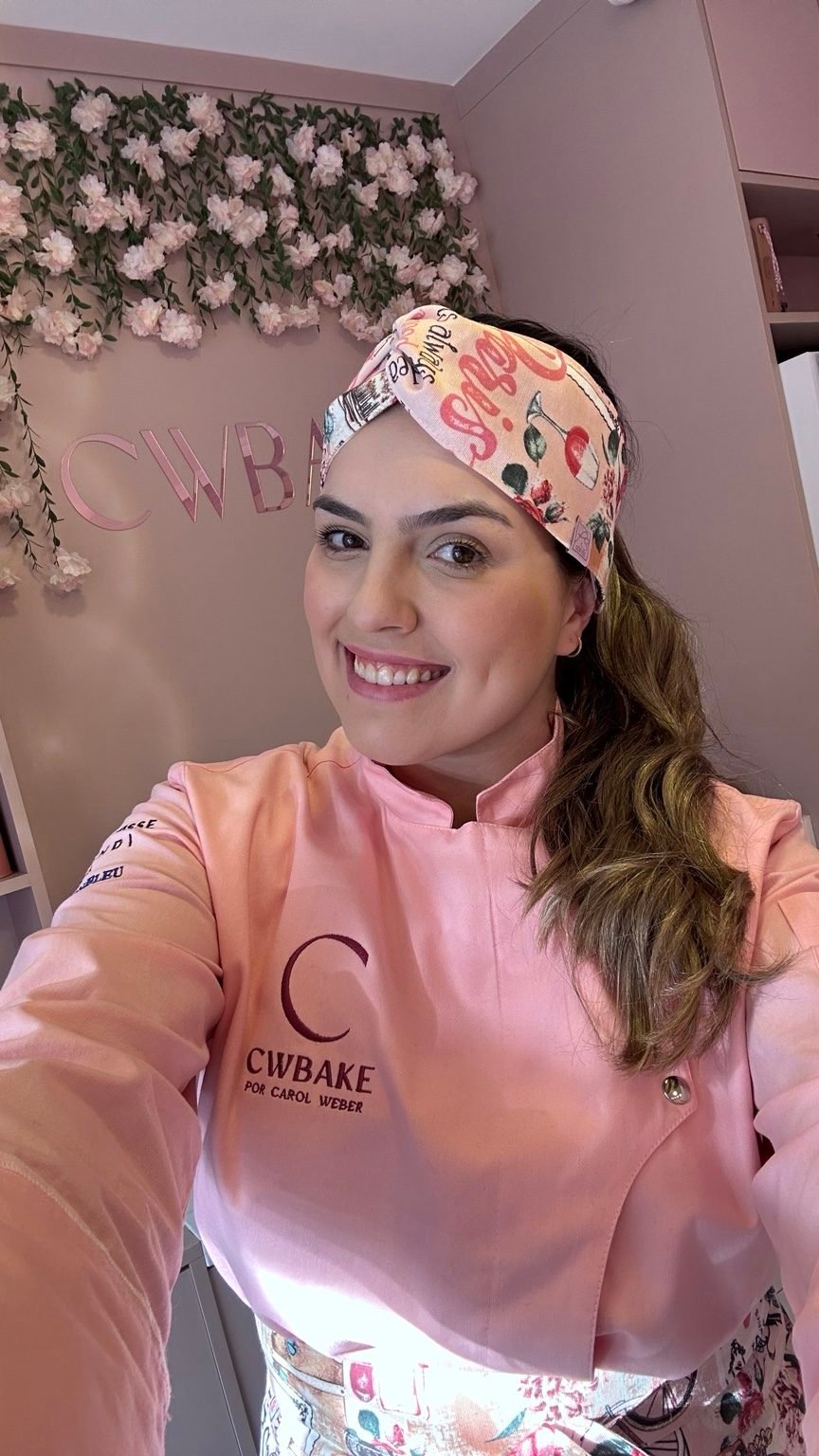 Chef Carol Weber Cantagalli, de dólmã rosa com o logo da CWBAKE
