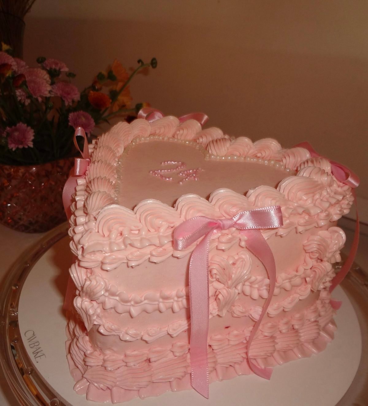 Bolo coração rosa com babados de buttercream, pérolas e laços de cetim, no prato da CWBAKE
