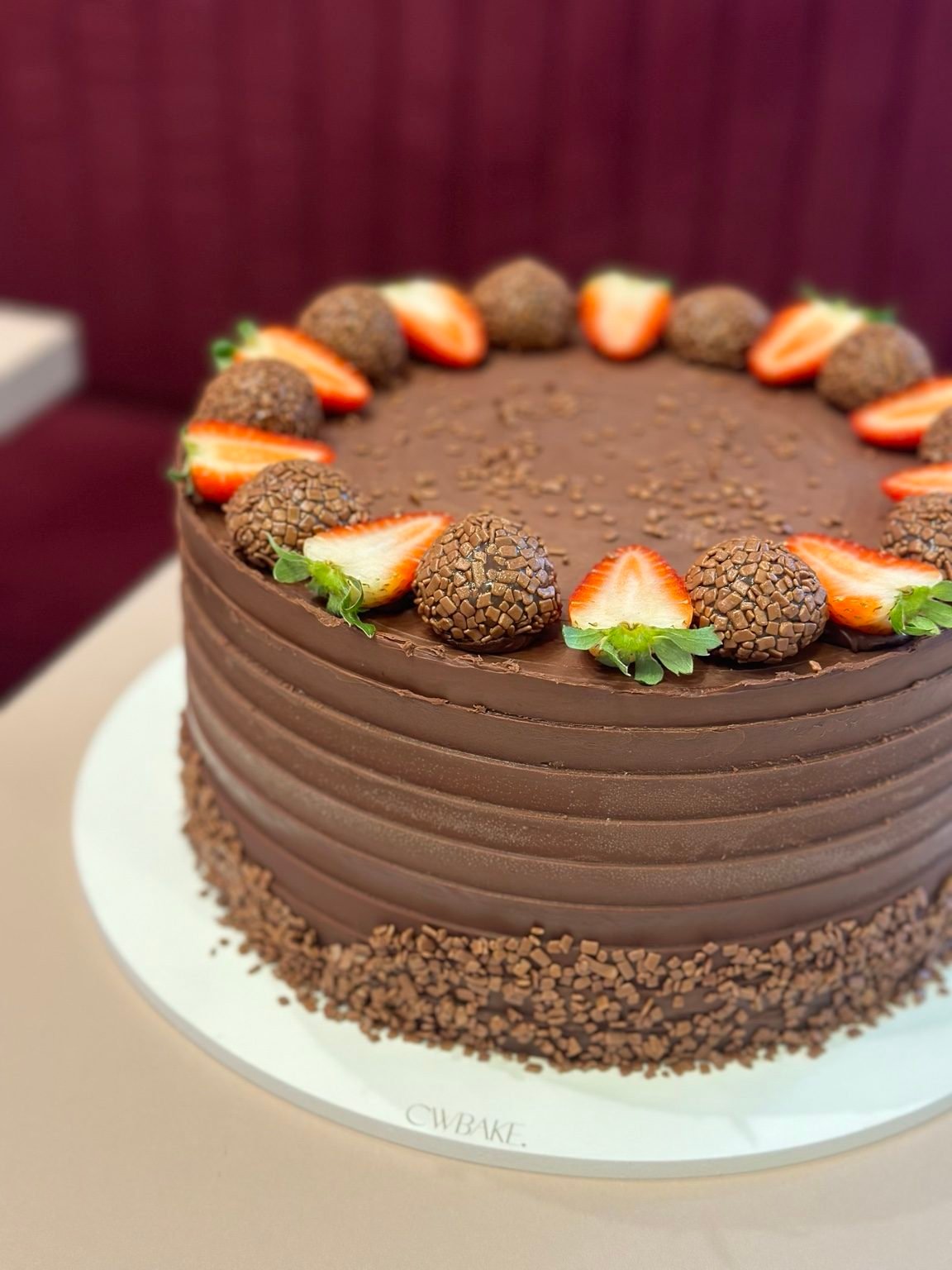 Bolo de chocolate com textura em faixas, morangos e brigadeiros no topo