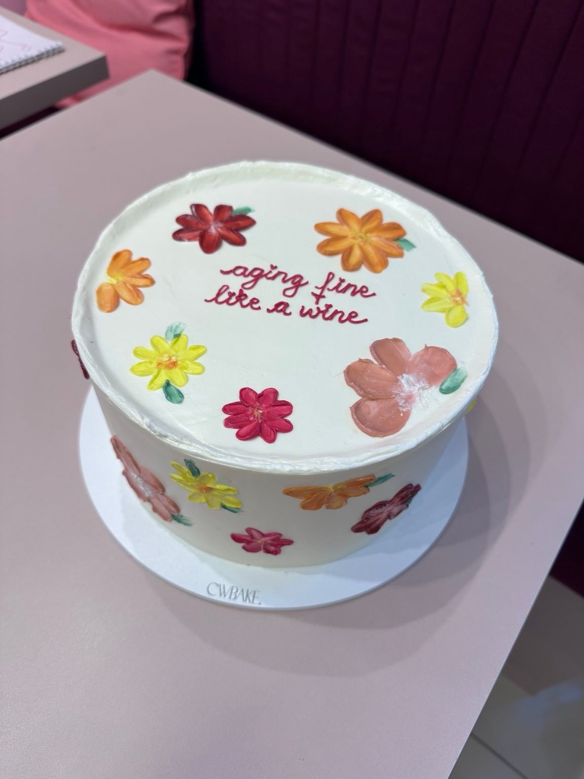Bolo branco com flores coloridas pintadas à mão e frase no topo